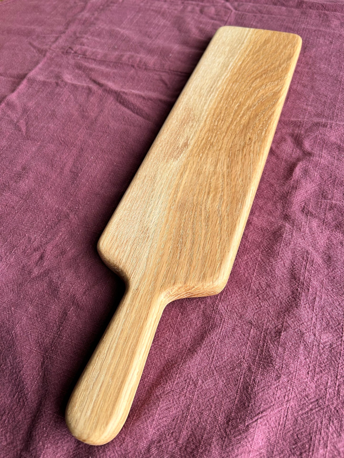 Wooden oak food serving board with a paddle style handle on a textured purple fabric background