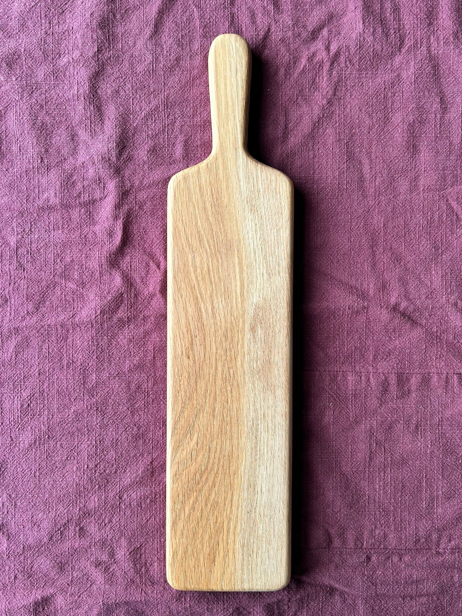 Oak wood charcuterie paddle on a purple fabric background