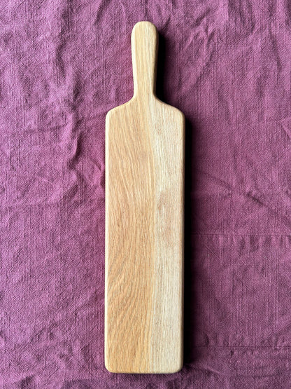 Oak wood charcuterie paddle on a purple fabric background