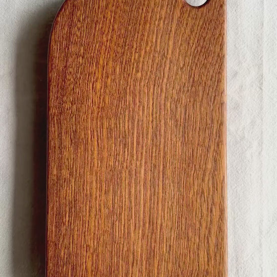 A video showing a brown cutting board made of sapele wood, on a white background