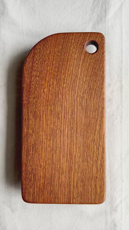 A video showing a brown cutting board made of sapele wood, on a white background
