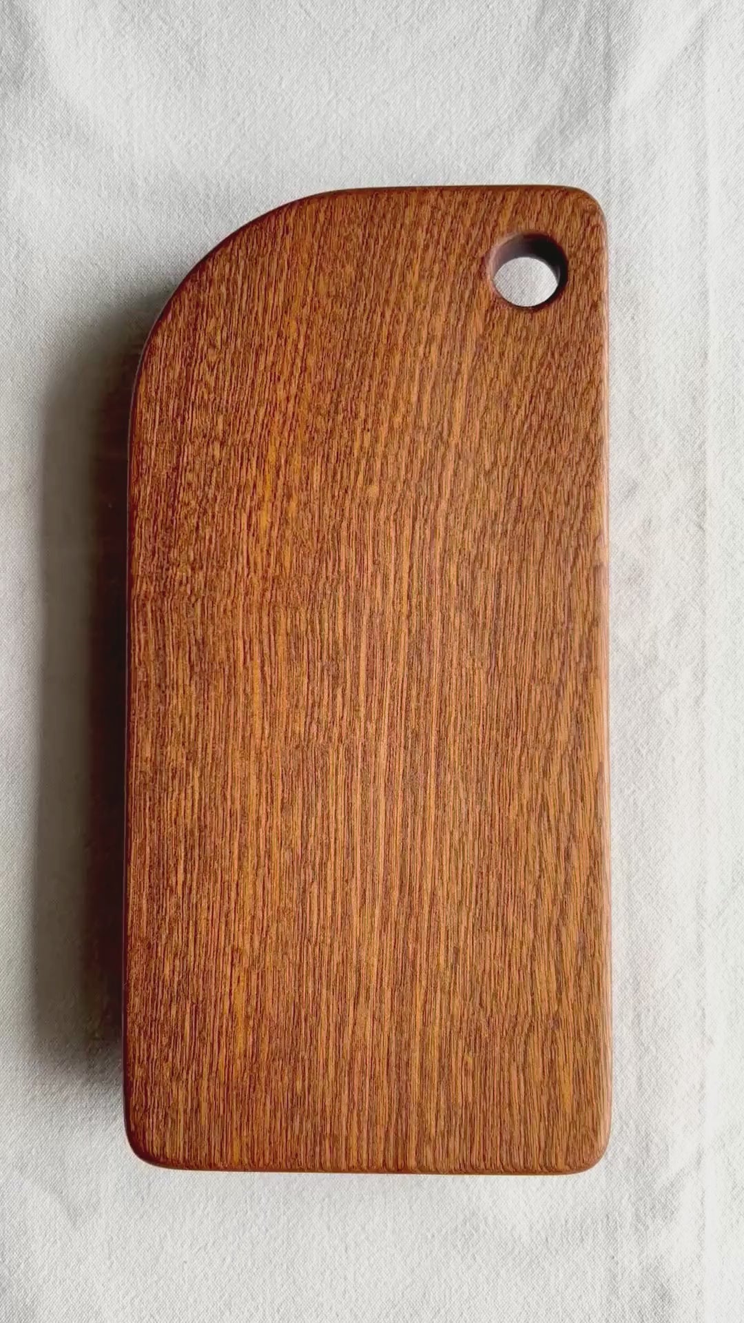 A video showing a brown cutting board made of sapele wood, on a white background