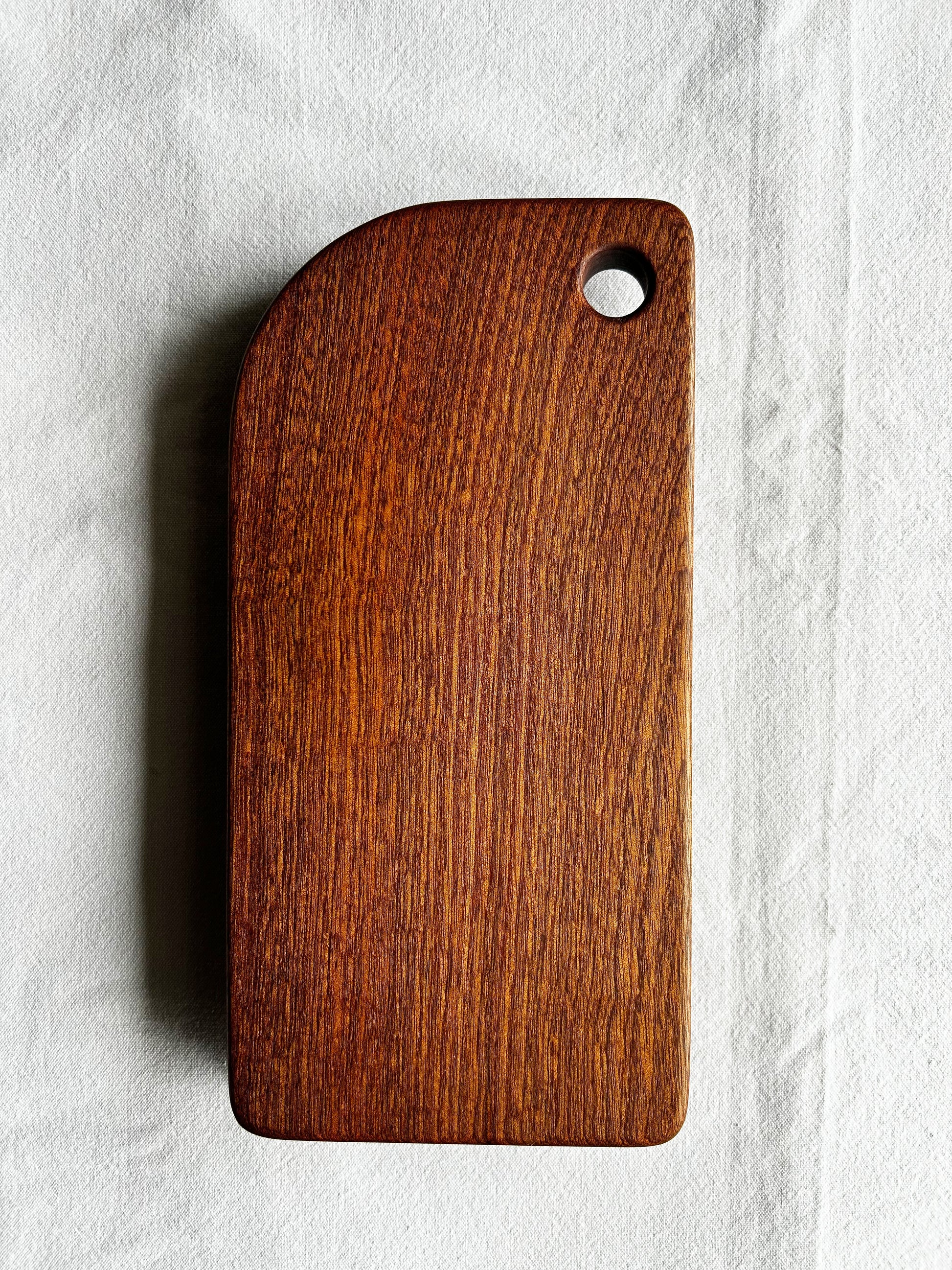 Wooden cutting board with a hole on a light grey background - wood is sapele