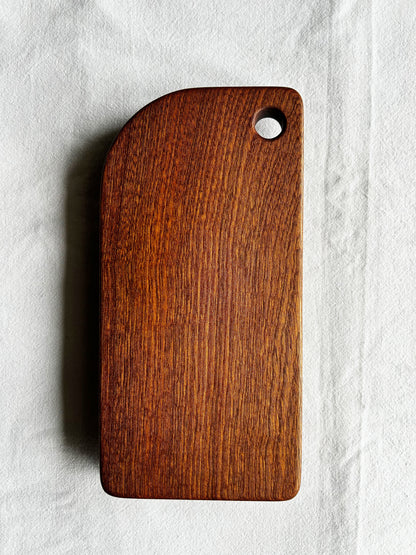 Wooden cutting board with a hole on a light grey background - wood is sapele