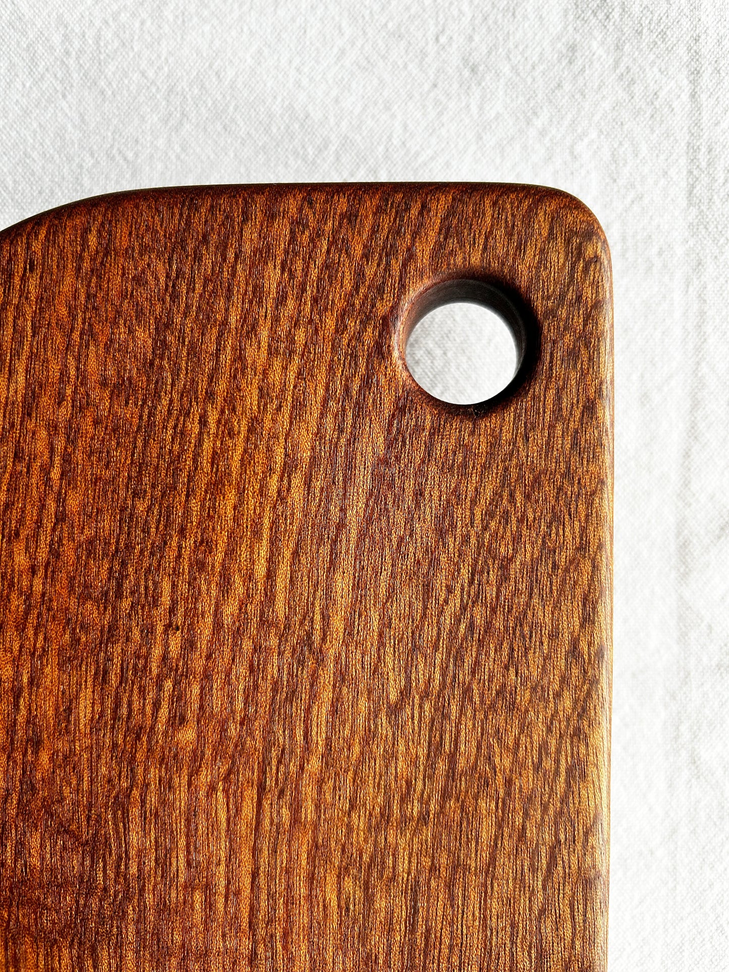 Brown wood cutting board with rounded edges and a finger hole handle on a white background