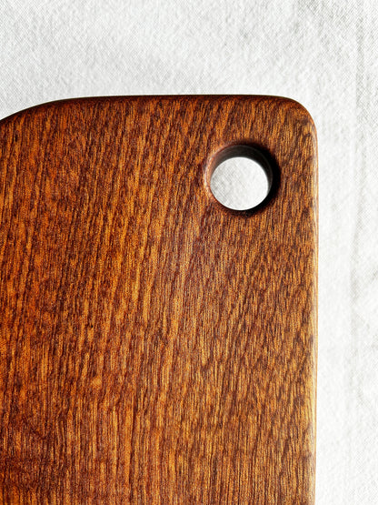 Brown wood cutting board with rounded edges and a finger hole handle on a white background