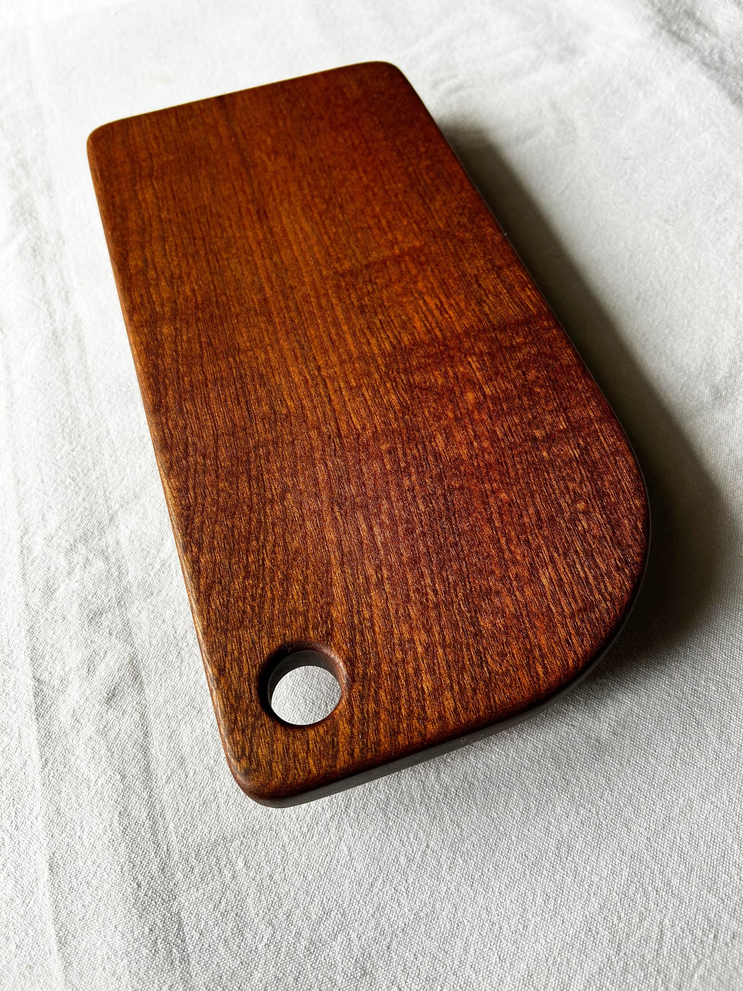 Small chocolate brown wooden cutting board with a hole on a light grey background