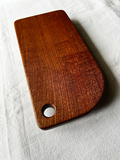 Small chocolate brown wooden cutting board with a hole on a light grey background