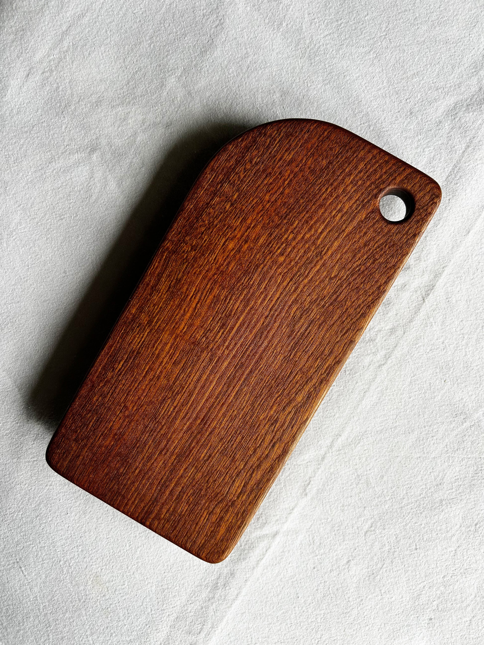 Chocolate brown wooden cutting board with a hole on a light grey background