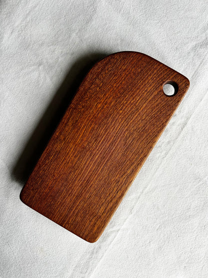 Chocolate brown wooden cutting board with a hole on a light grey background