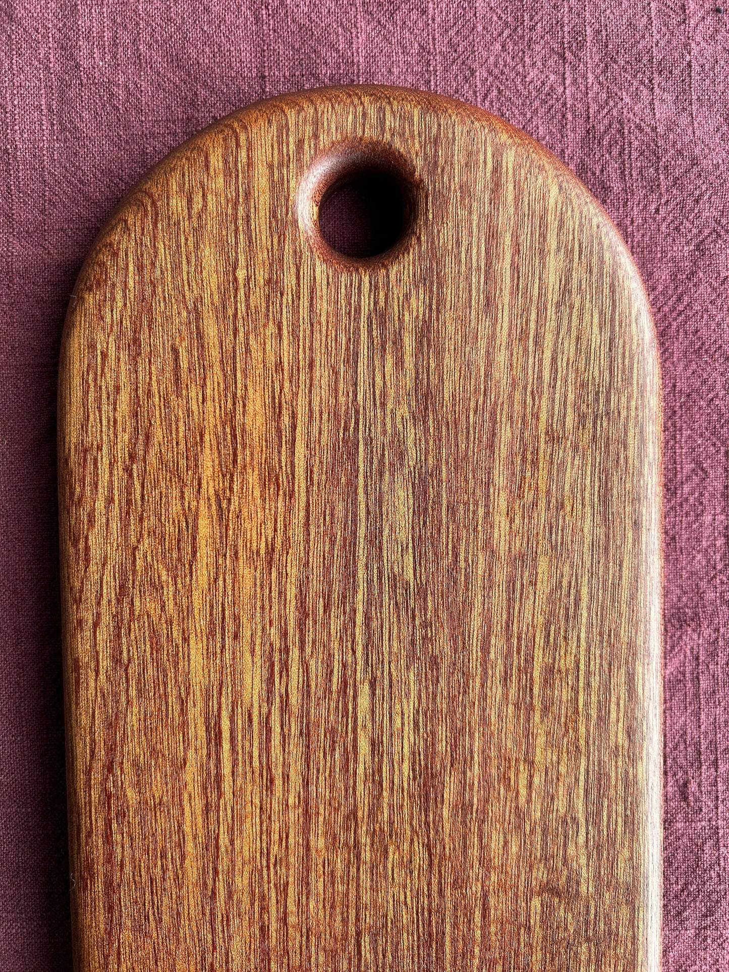Close-up of a sapele wooden cutting board with a hole for a handle on a purple textured background