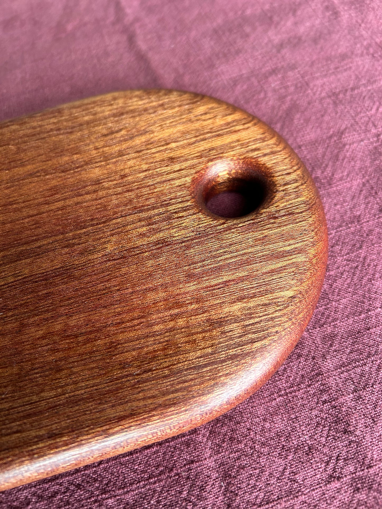 Sapele wooden rounded serving board with a hole on a purple fabric background