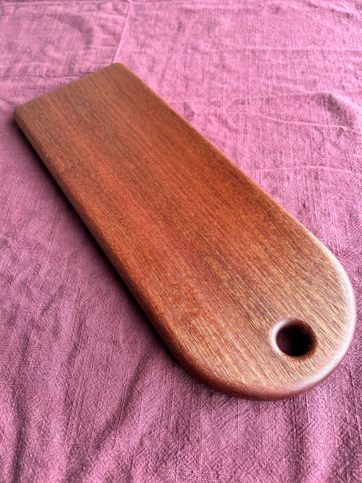 Wooden charcuterie board with a hole on a purple fabric background