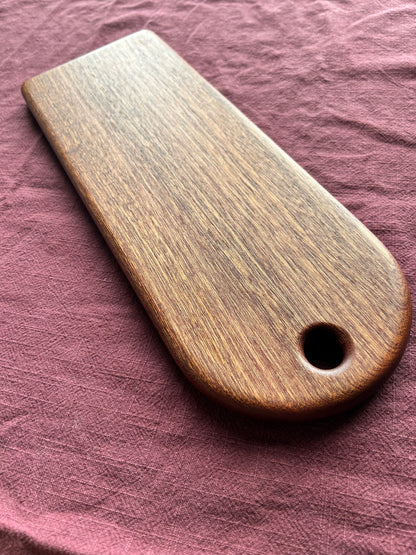 Dark brown wooden food serving board with a hole on a pink fabric background